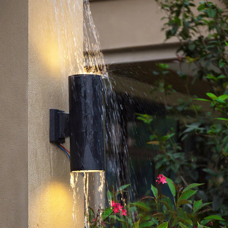 Water running over a lit cylinder light on an outdoor wall, a splash test