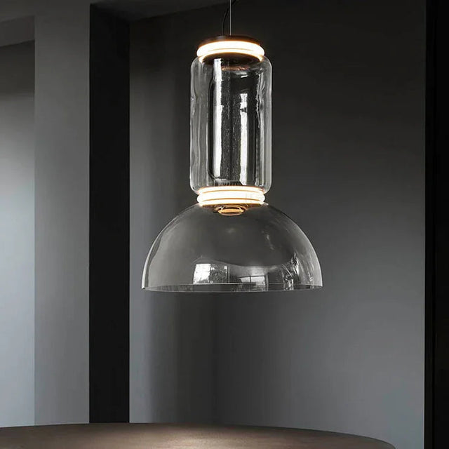 The stacked glass cylinder pendant lit against a dark painted wall