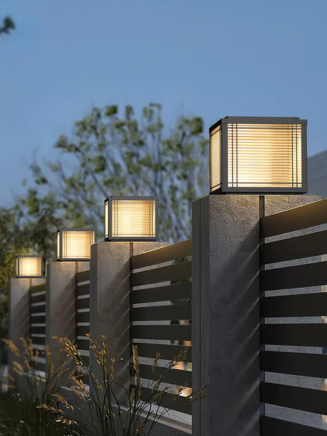 Lit cap on a fence post with trees and a timber slat panel behind it