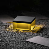 The flat box lit low on a gravel border beside a paving slab at night