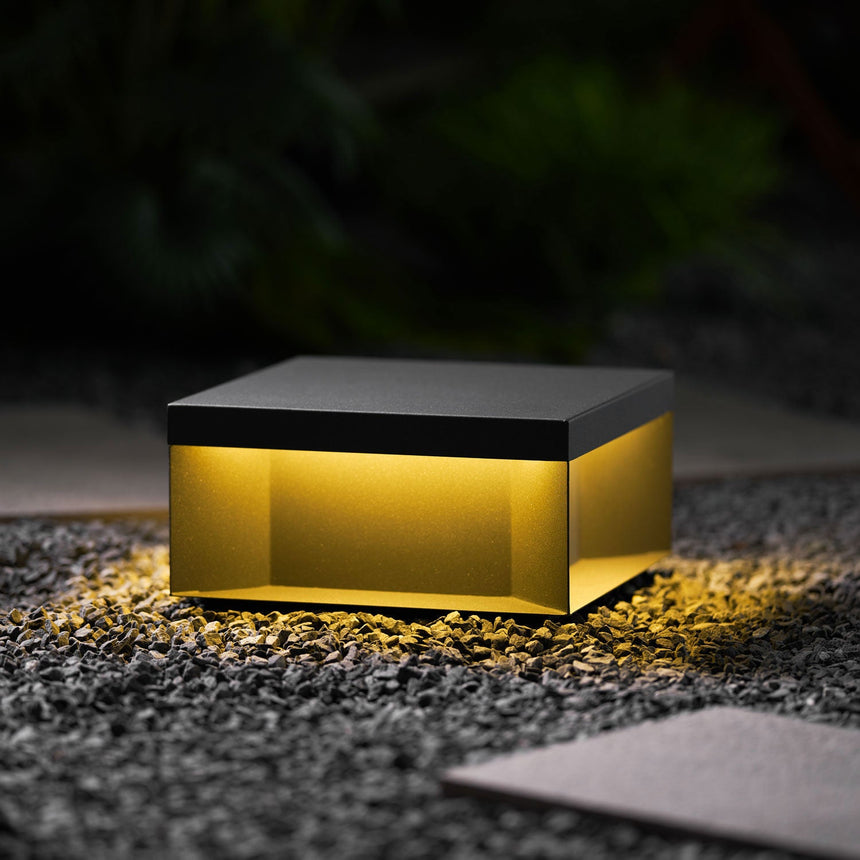 Light spilling from under the box onto gravel and a paving stone at night