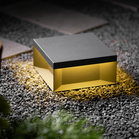 The box lit on gravel with low planting behind it in a dark garden