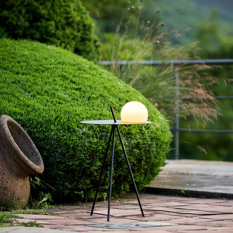 The tripod table lit on paving beside a clipped hedge and a stone pot