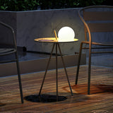 The tripod table lit on a timber deck beside a chair and a round rug