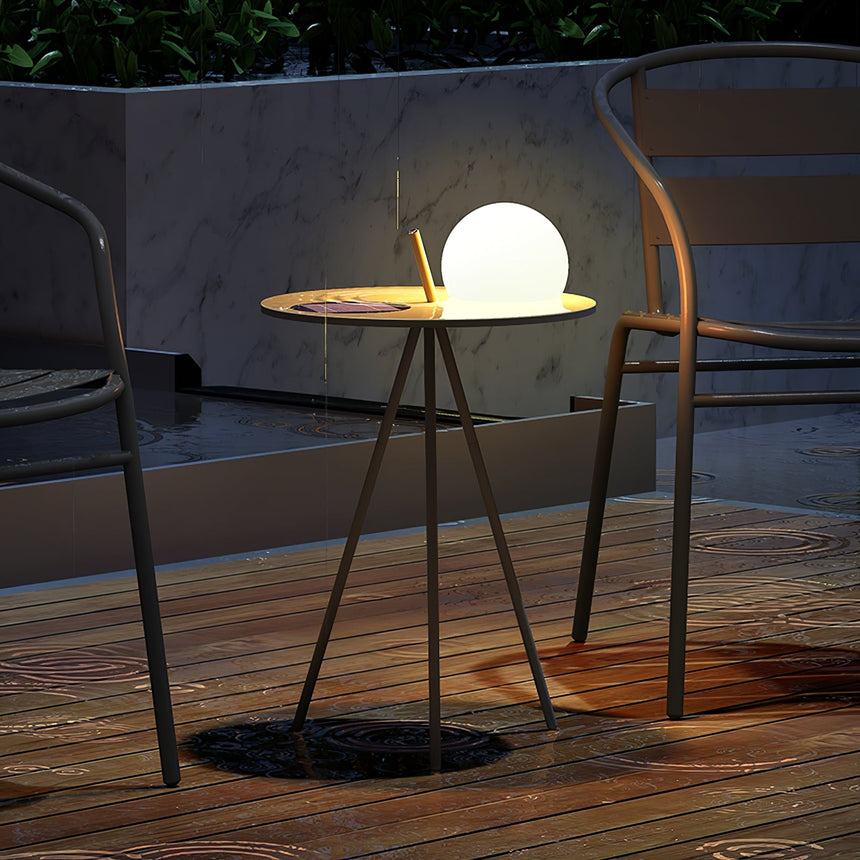 The tripod table lit on a timber deck beside a chair and a round rug