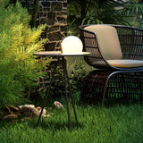 The tripod table lit on a lawn beside a woven armchair and planting
