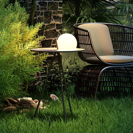 The tripod table lit on a lawn beside a woven armchair and planting
