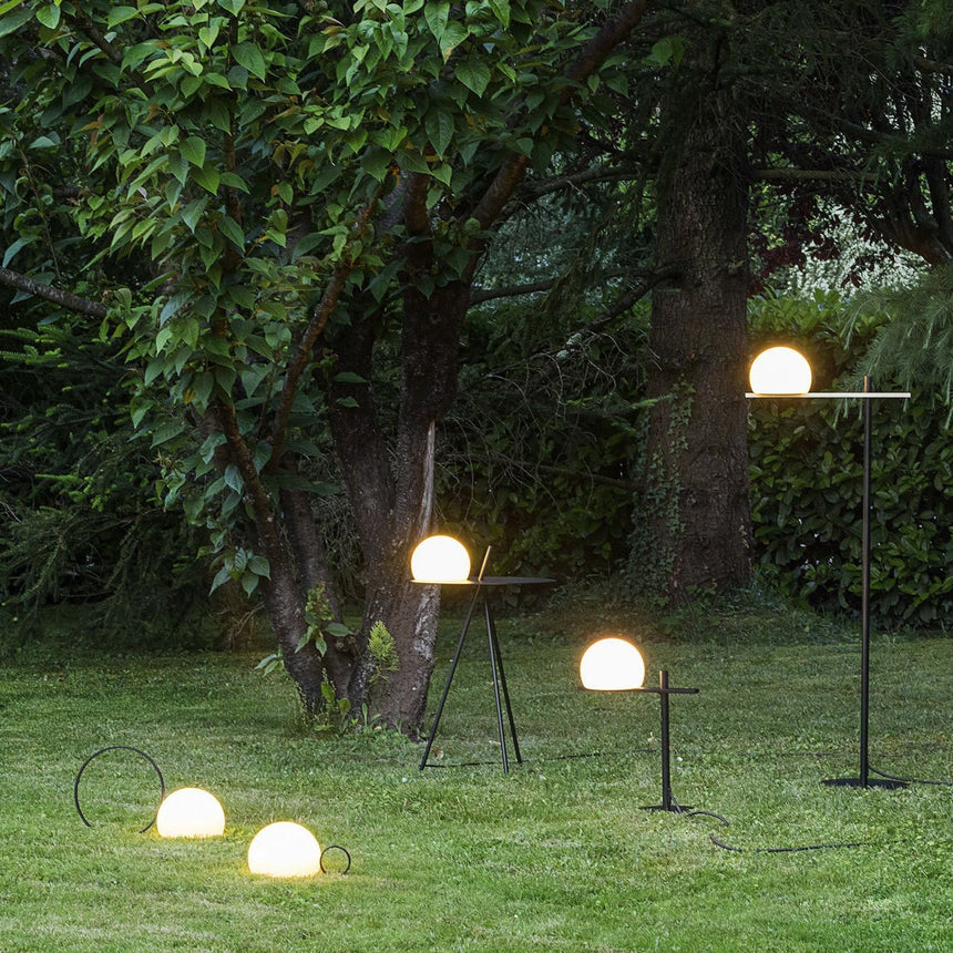 Several lit globes set along a lawn under trees with a tripod among them