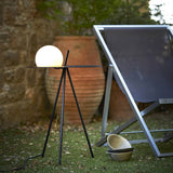 The tripod table lit beside a stone wall with a terracotta pot behind