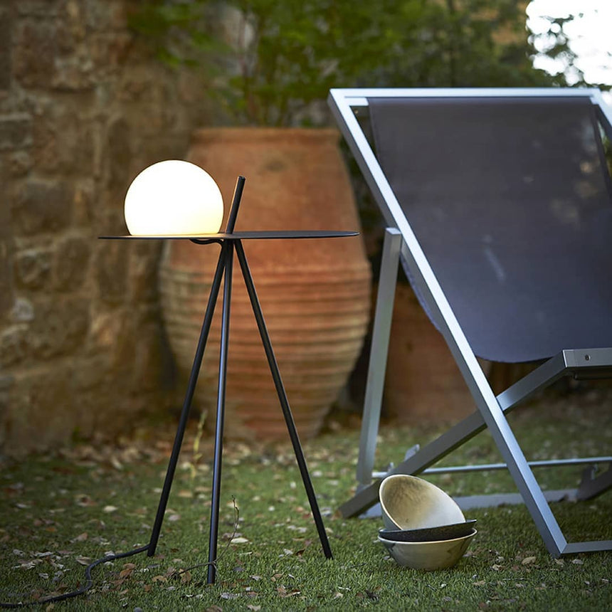 The tripod table lit beside a stone wall with a terracotta pot behind
