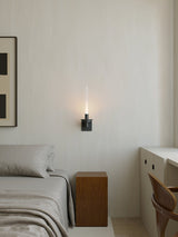 Lit in a bedroom between a framed print, a made bed and a small desk