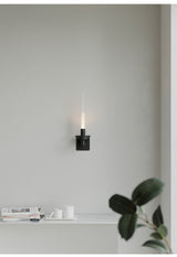 Lit above a white shelf holding a small plant, a stack of books and a tray