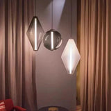 A diamond and two sphere pendants lit in front of a long curtain beside a chair