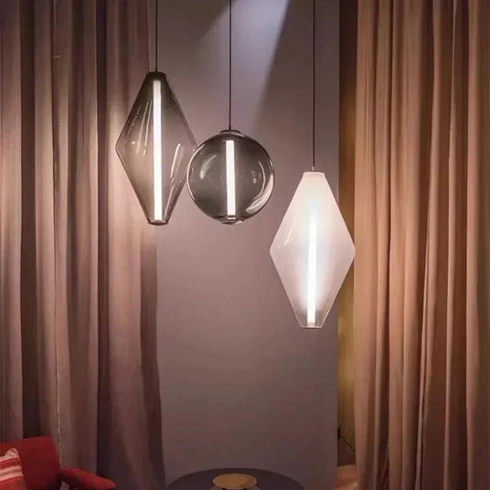 A diamond and two sphere pendants lit in front of a long curtain beside a chair