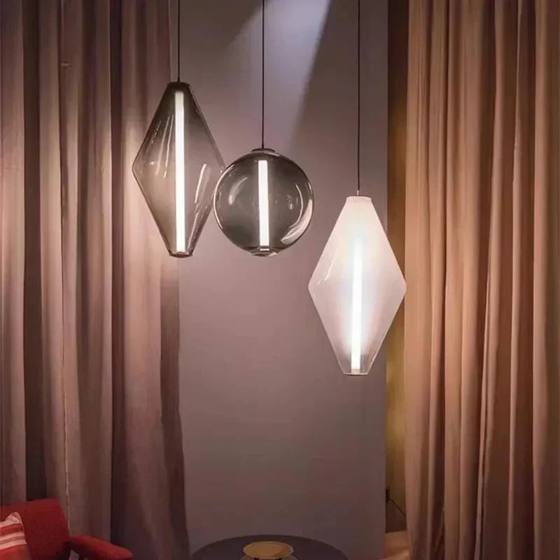 A diamond and two sphere pendants lit in front of a long curtain beside a chair