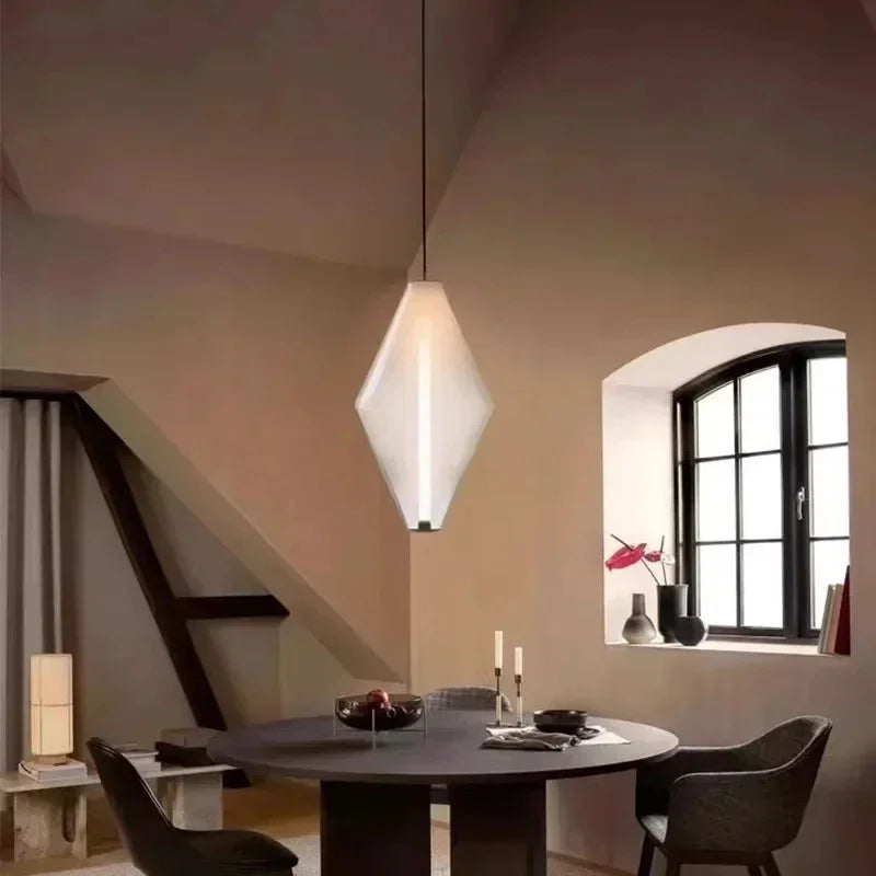 A diamond pendant lit in a tall stairwell beside an arched window and a table