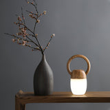 Dimmable bedside lamp lit on a wooden console beside a tall stone vase