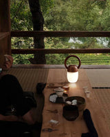 Dimmable bedside lamp lit on a long wooden table set with bowls