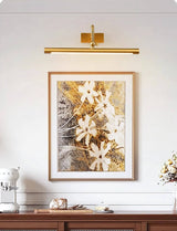 Brass bar lit over a framed canvas above a dark wood console with vases