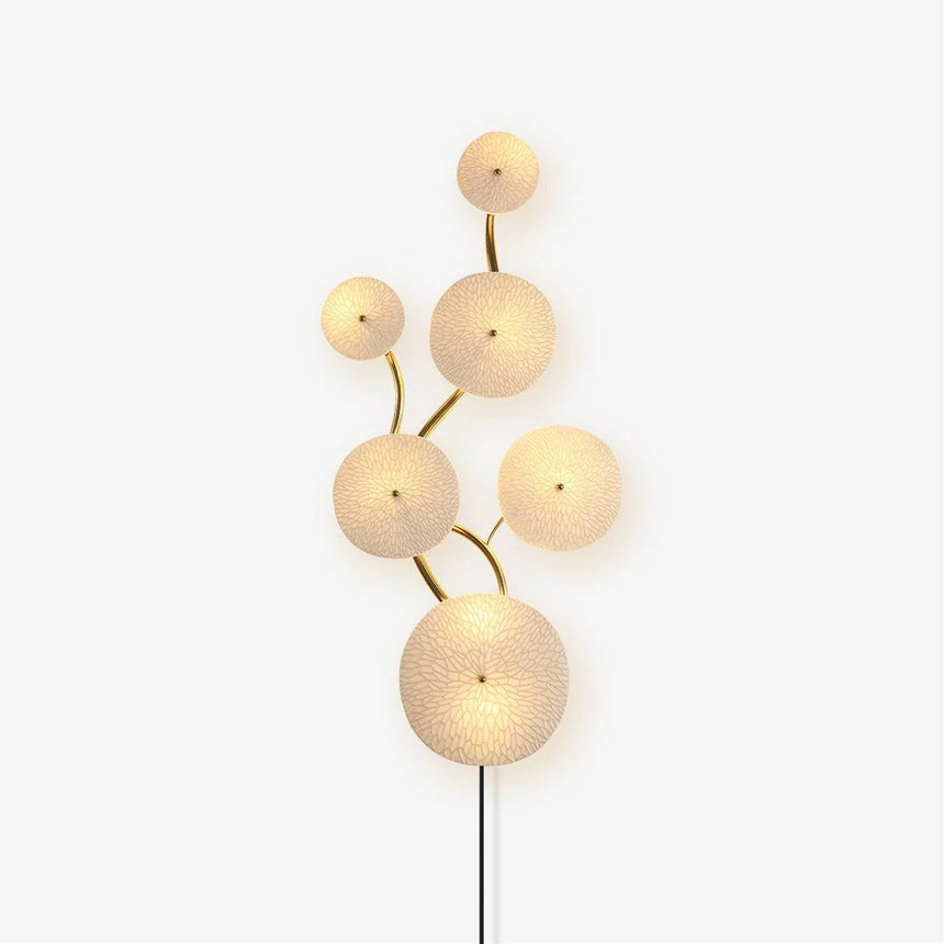 Plug in wall light of textured white ceramic discs on a gold stem, the cord running down