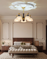 Chandelier lit in a bedroom above a bed with a padded headboard