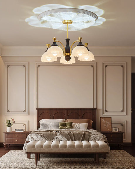 Chandelier lit in a bedroom above a bed with a padded headboard