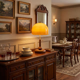 Amber dome table lamp lit on a sideboard in a dining room with pictures