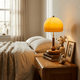 Amber dome table lamp lit on a nightstand beside a made bed