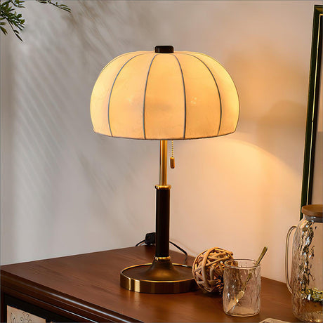 Segmented dome lamp lit on a console beside a glass and a woven ball