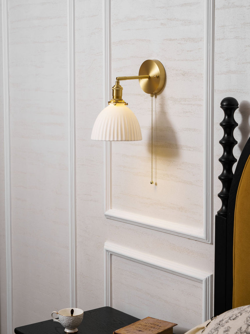The sconce on a white paneled wall beside a dark turned wood bed