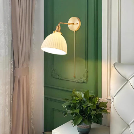 The sconce lit on a green paneled wall beside a curtain and a potted plant