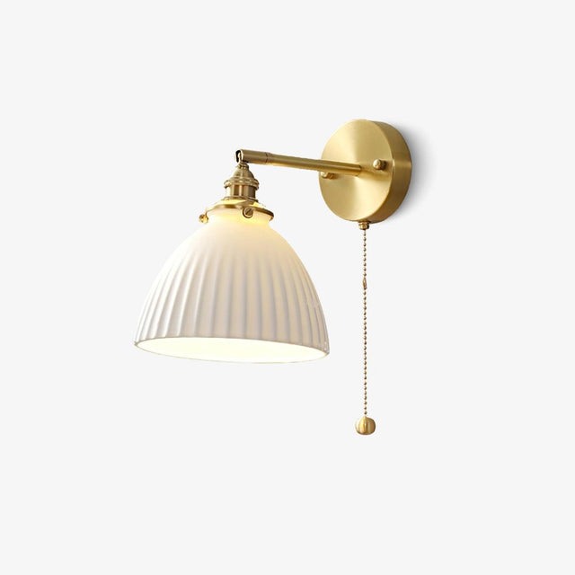 Brass wall sconce with a pleated white ceramic dome shade and a brass pull chain