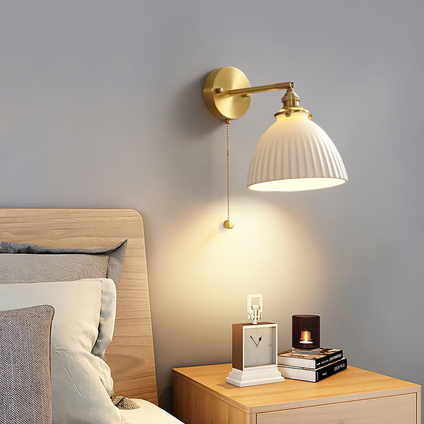 The dome sconce lit above a wood nightstand with a clock and a candle beside a bed