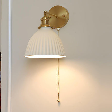 The sconce lit above a leafy plant, light pooling on the wall