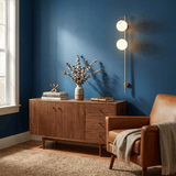 The lit sconce on a deep blue wall above a cabinet and an armchair