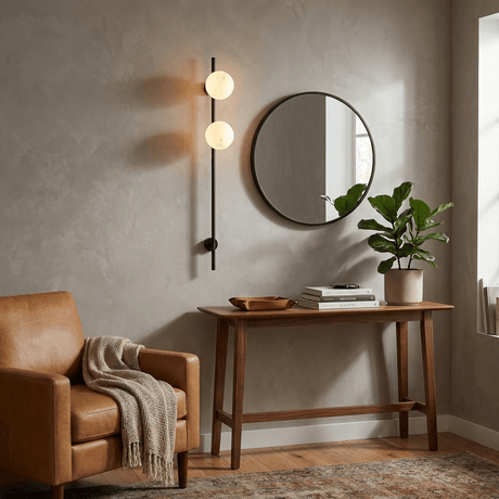 The lit sconce beside a round mirror above a console in an entry