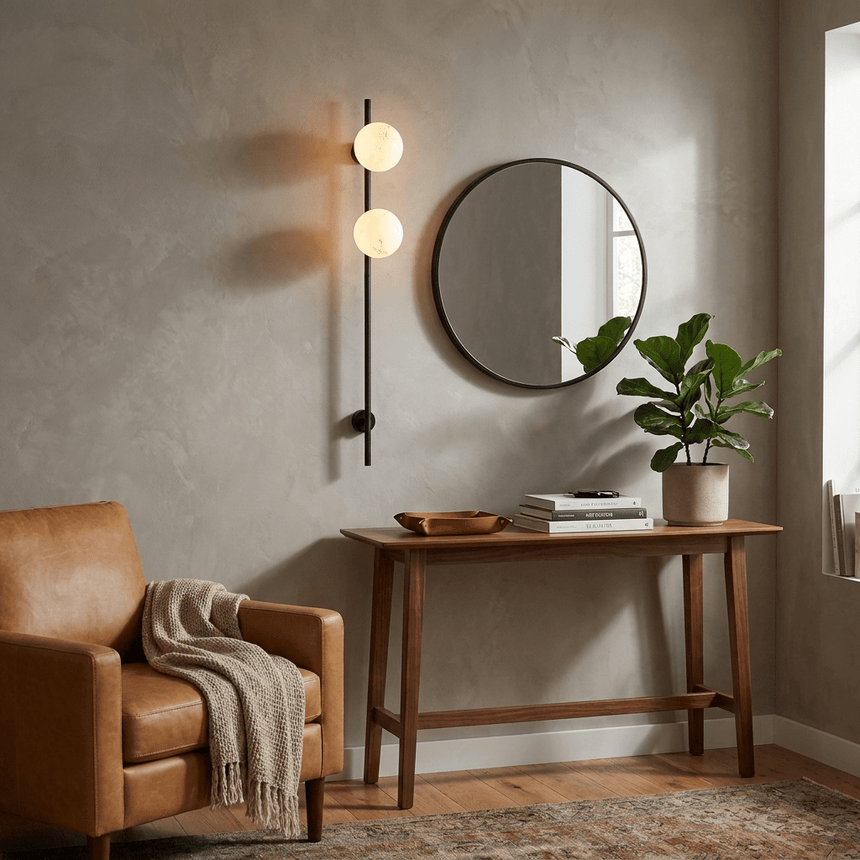 The lit sconce beside a round mirror above a console in an entry