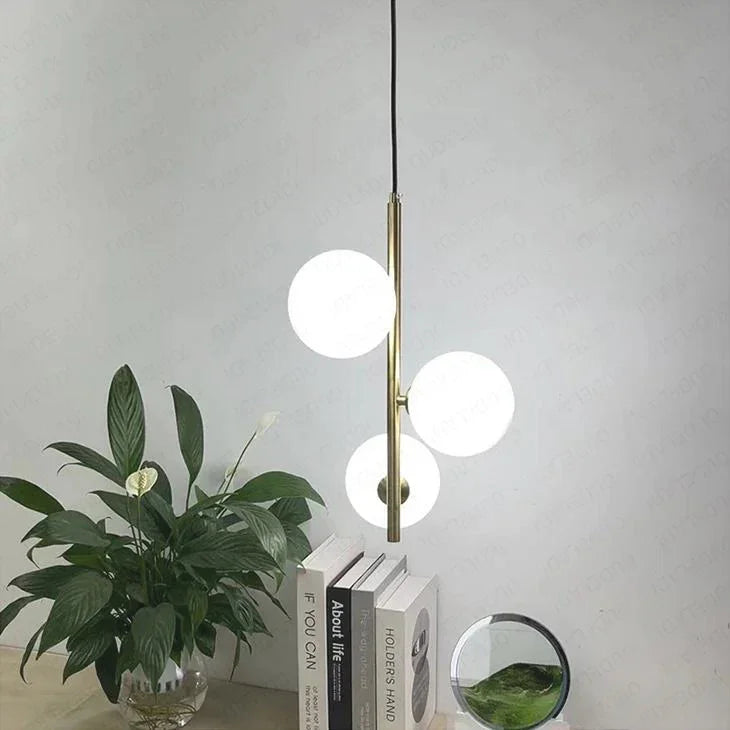 Three opal globes on brass stems above a shelf of books and a plant