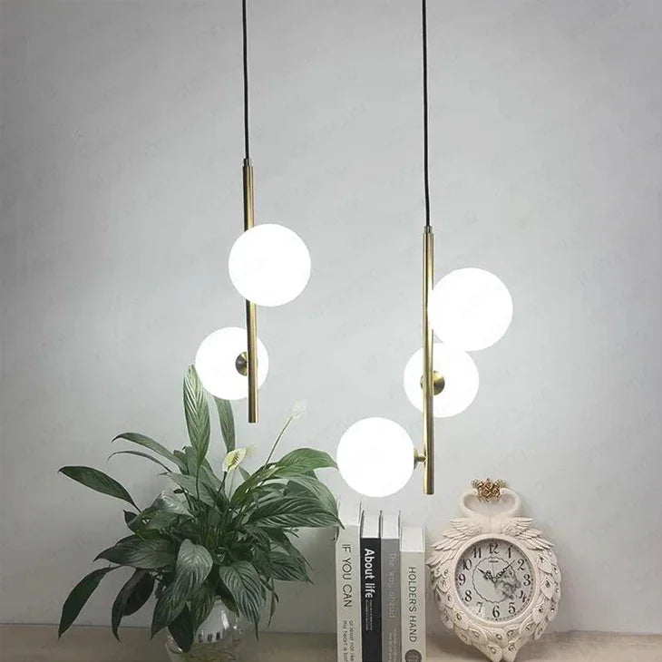 Two opal globes on slim brass stems beside a green plant and a clock