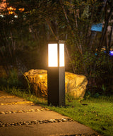 The bollard lit on a stone path beside a boulder and tall grasses