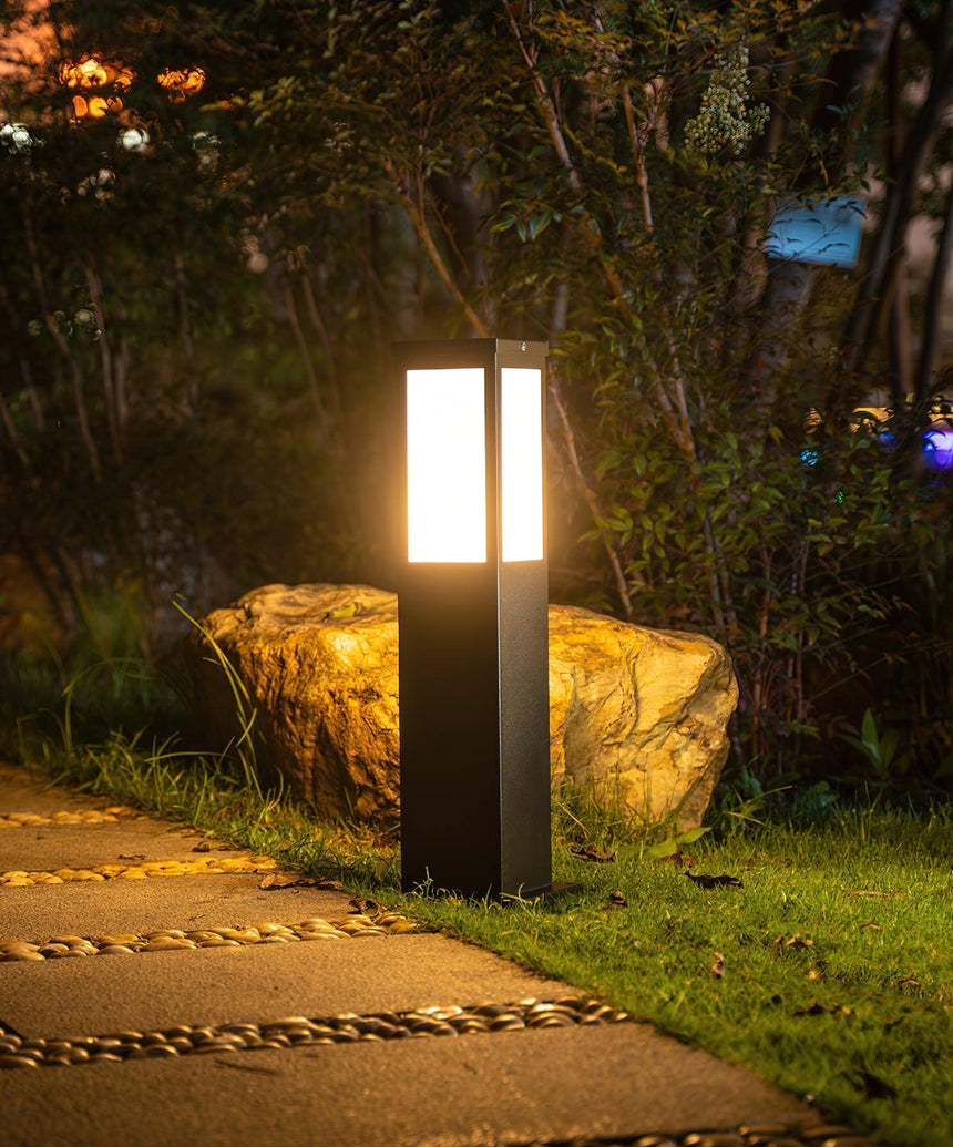 The bollard lit on a stone path beside a boulder and tall grasses