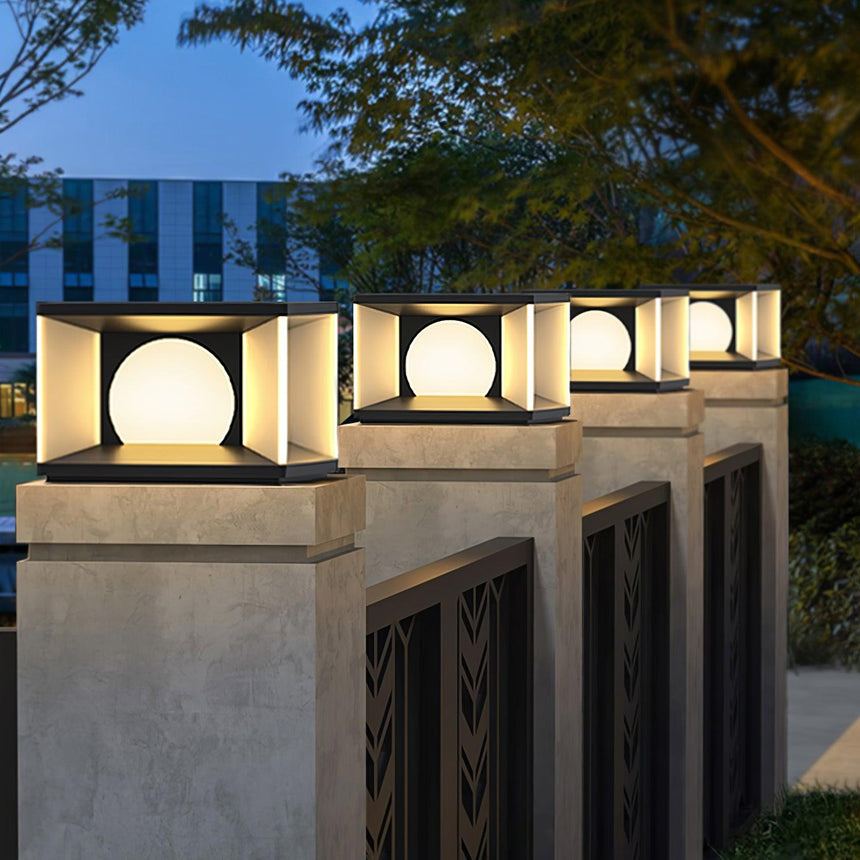 Lit cubes on pillars beside a white fence and a planted driveway edge