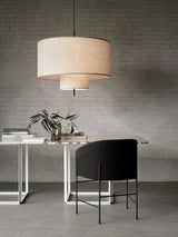 Drum shade pendant light above a small side table and a dark chair