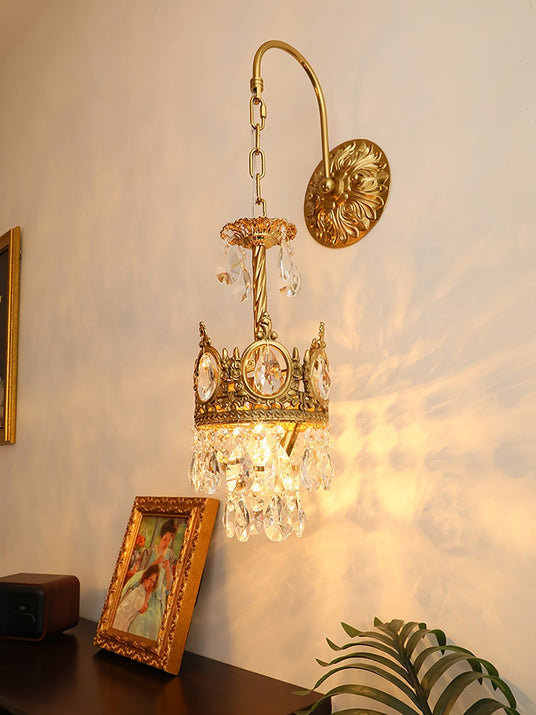 The sconce lit above a dark console with a framed picture and a plant