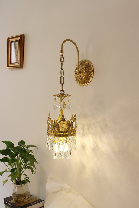 The sconce lit above a potted plant beside a small framed mirror