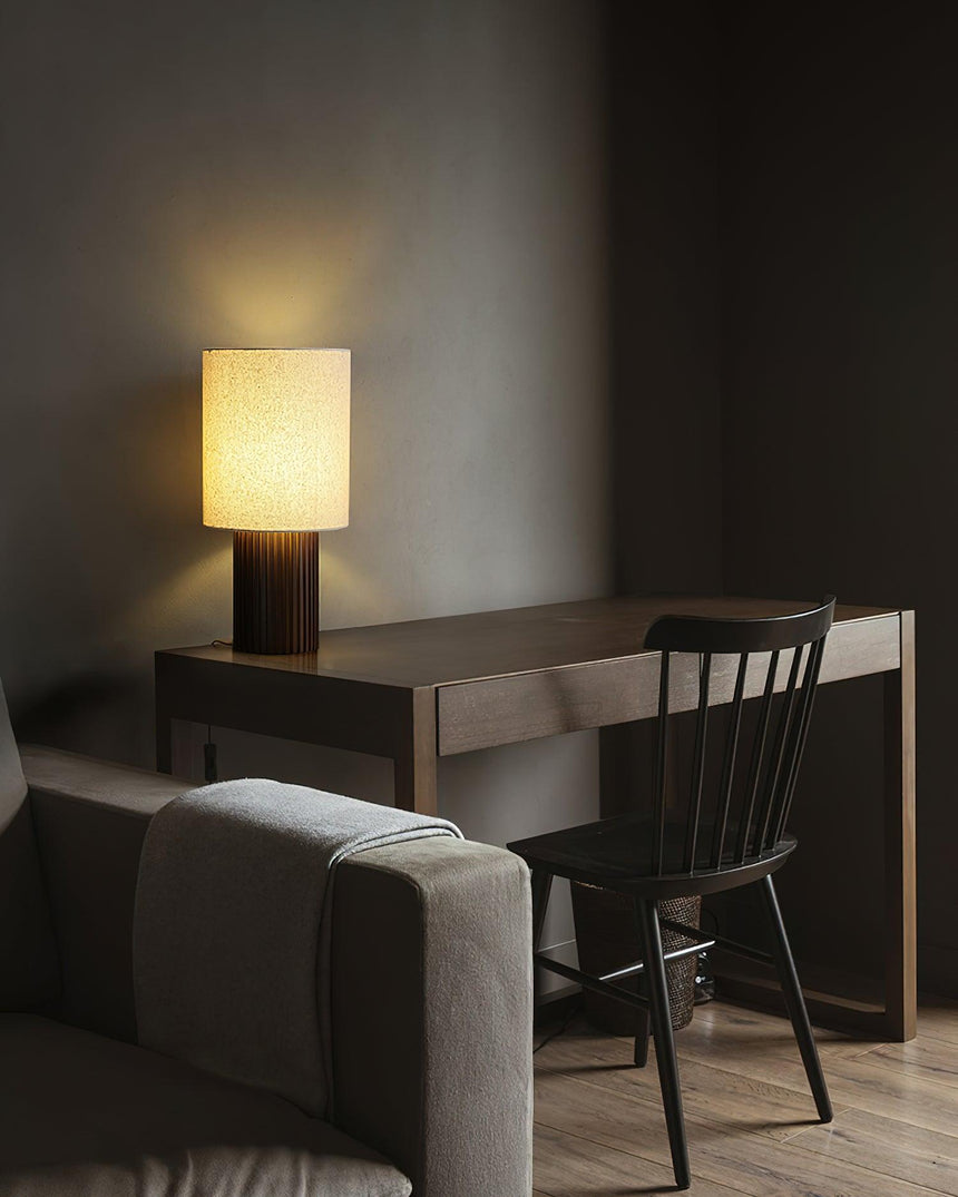 Entryway table lamp lit on a desk in a study with a dark chair