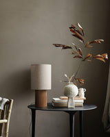 Entryway table lamp unlit on a round table beside a vase of branches