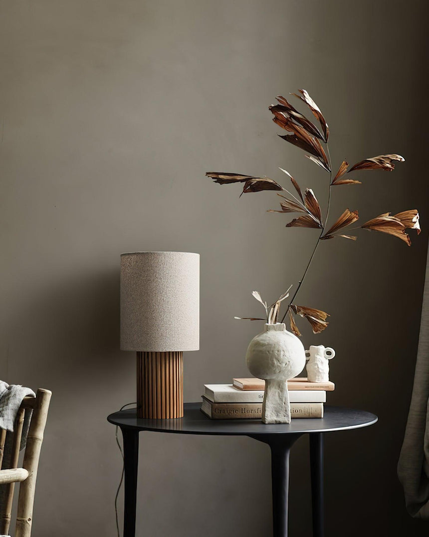Entryway table lamp unlit on a round table beside a vase of branches