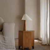 Wood cone lamp unlit on a wood stool beside a pale armchair