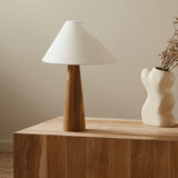 Wood cone lamp unlit on a wood block in a corner beside a vase